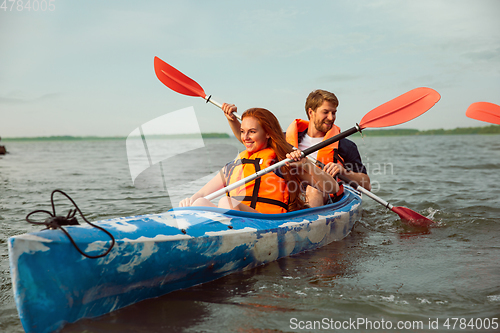 Image of Happy couple kayaking on river with sunset on the background