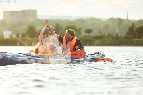 Image of Happy couple kayaking on river with sunset on the background