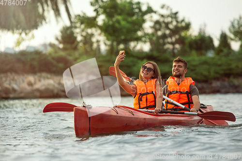 Image of Happy couple kayaking on river with sunset on the background