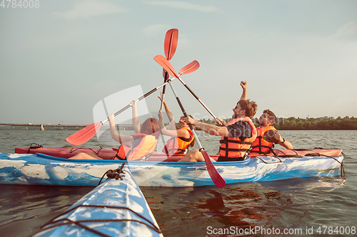 Image of Happy friends kayaking on river with sunset on the background