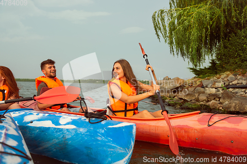 Image of Happy friends kayaking on river with sunset on the background