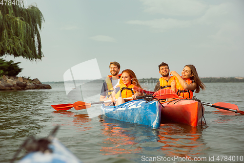 Image of Happy friends kayaking on river with sunset on the background