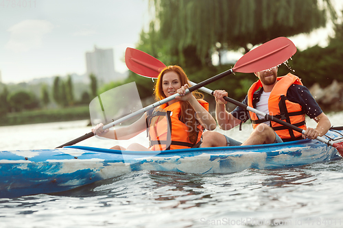 Image of Happy couple kayaking on river with sunset on the background