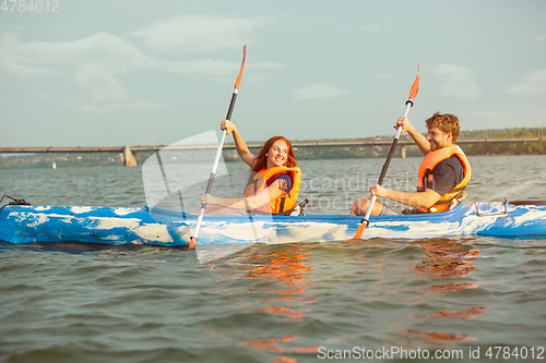 Image of Happy couple kayaking on river with sunset on the background