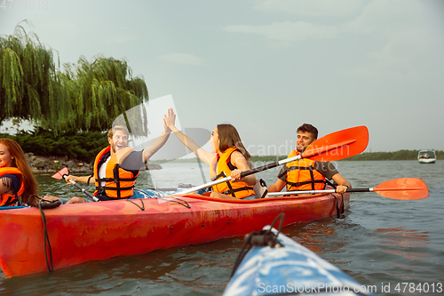 Image of Happy friends kayaking on river with sunset on the background