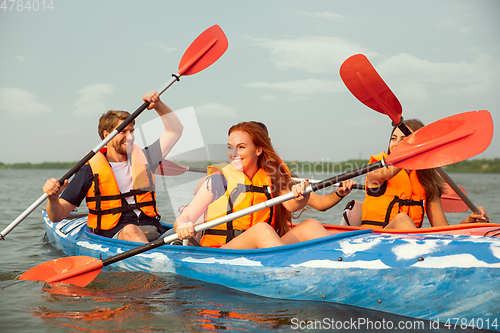 Image of Happy friends kayaking on river with sunset on the background