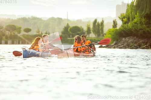 Image of Happy friends kayaking on river with sunset on the background