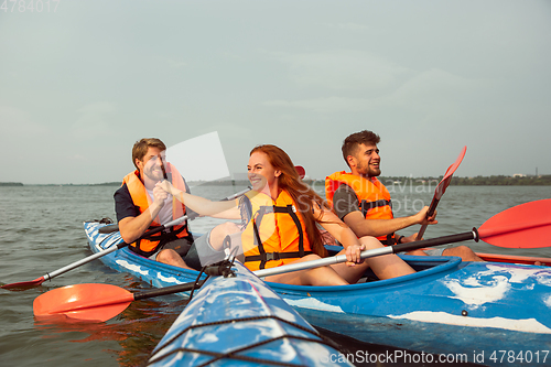 Image of Happy friends kayaking on river with sunset on the background