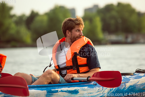 Image of Caucasian man kayaking on river with sunset on the background