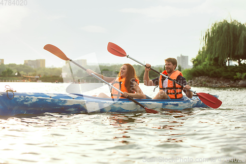 Image of Happy couple kayaking on river with sunset on the background