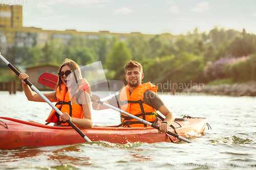 Image of Happy couple kayaking on river with sunset on the background