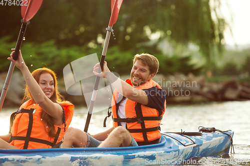 Image of Happy couple kayaking on river with sunset on the background