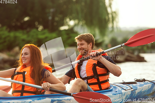 Image of Happy couple kayaking on river with sunset on the background