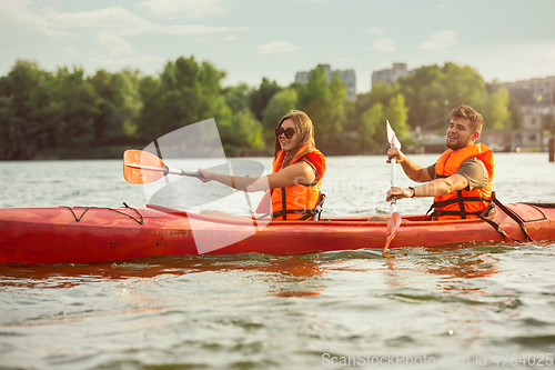 Image of Happy couple kayaking on river with sunset on the background