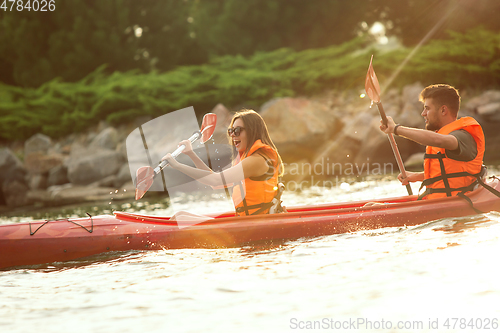 Image of Happy couple kayaking on river with sunset on the background