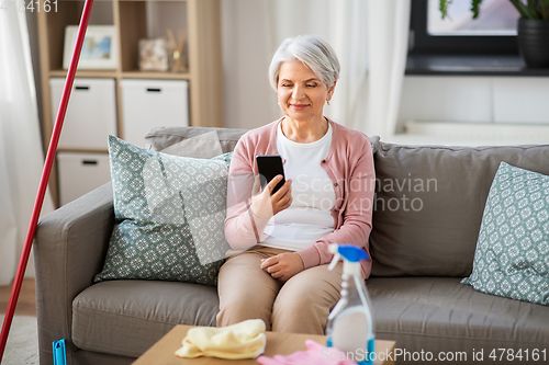 Image of senior woman using smartphone after cleaning home