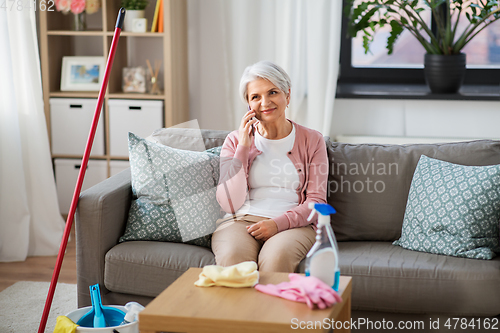 Image of old woman calling on cellphone after cleaning home