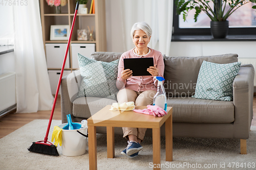 Image of senior woman using tablet pc after cleaning home