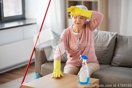 Image of tired senior woman cleaning table at home