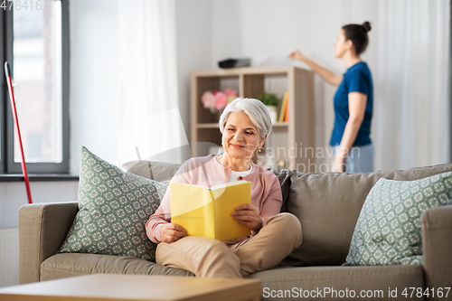 Image of old woman reading book and housekeeper at home