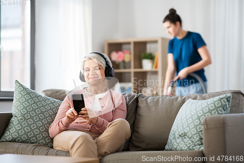 Image of old woman in headphones with smartphone at home