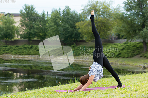 Image of Young beautiful woman doing yoga exercise in green park. Healthy lifestyle and fitness concept.