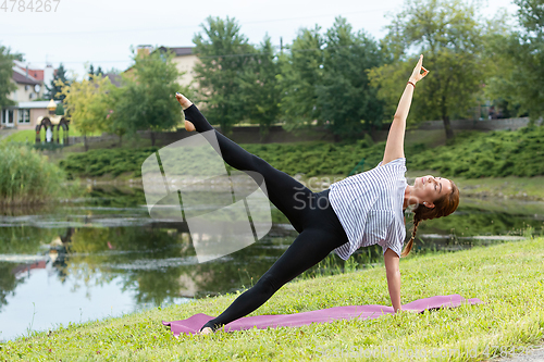 Image of Young beautiful woman doing yoga exercise in green park. Healthy lifestyle and fitness concept.