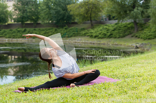 Image of Young beautiful woman doing yoga exercise in green park. Healthy lifestyle and fitness concept.