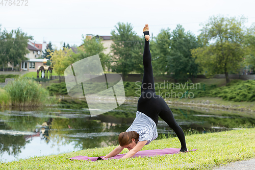 Image of Young beautiful woman doing yoga exercise in green park. Healthy lifestyle and fitness concept.