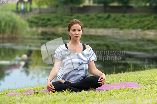 Image of Young beautiful woman doing yoga exercise in green park. Healthy lifestyle and fitness concept.