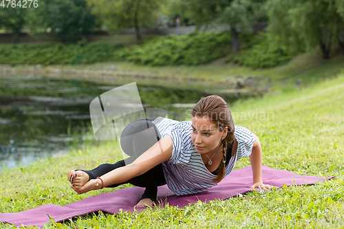 Image of Young beautiful woman doing yoga exercise in green park. Healthy lifestyle and fitness concept.