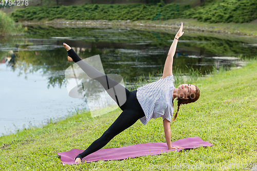 Image of Young beautiful woman doing yoga exercise in green park. Healthy lifestyle and fitness concept.