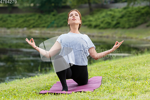 Image of Young beautiful woman doing yoga exercise in green park. Healthy lifestyle and fitness concept.