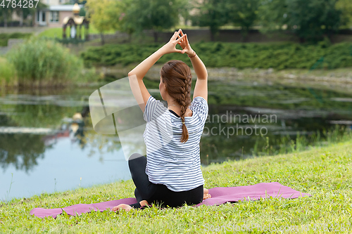 Image of Young beautiful woman doing yoga exercise in green park. Healthy lifestyle and fitness concept.