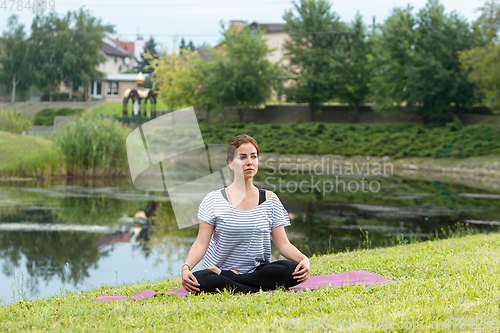 Image of Young beautiful woman doing yoga exercise in green park. Healthy lifestyle and fitness concept.