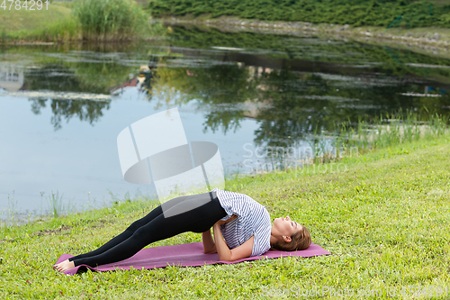 Image of Young beautiful woman doing yoga exercise in green park. Healthy lifestyle and fitness concept.