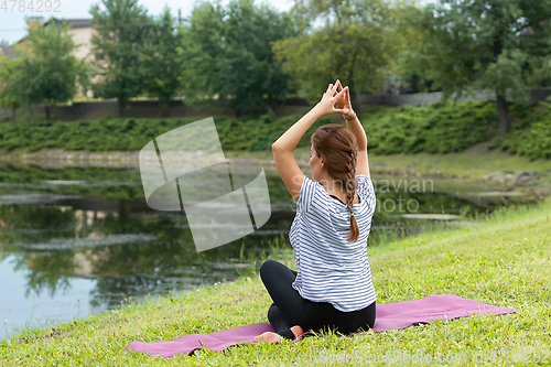 Image of Young beautiful woman doing yoga exercise in green park. Healthy lifestyle and fitness concept.