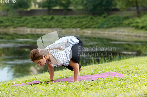 Image of Young beautiful woman doing yoga exercise in green park. Healthy lifestyle and fitness concept.