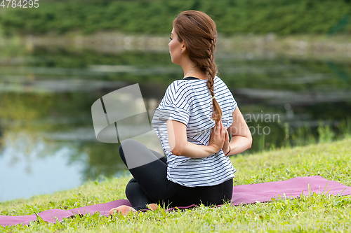 Image of Young beautiful woman doing yoga exercise in green park. Healthy lifestyle and fitness concept.