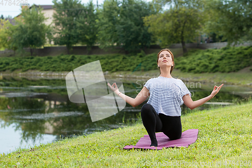 Image of Young beautiful woman doing yoga exercise in green park. Healthy lifestyle and fitness concept.