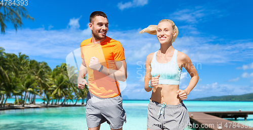 Image of smiling couple running along exotic on beach