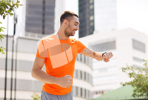 Image of smiling young man with smart watch running at city