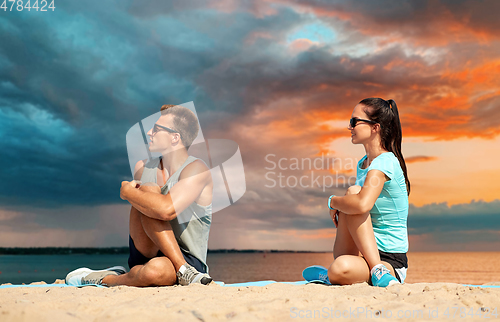 Image of smiling couple stretching legs on beach