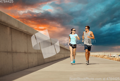 Image of couple in sports clothes running along pier