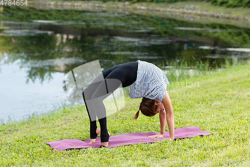 Image of Young beautiful woman doing yoga exercise in green park. Healthy lifestyle and fitness concept.