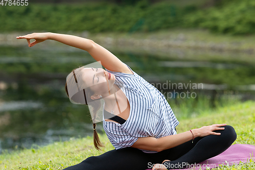 Image of Young beautiful woman doing yoga exercise in green park. Healthy lifestyle and fitness concept.