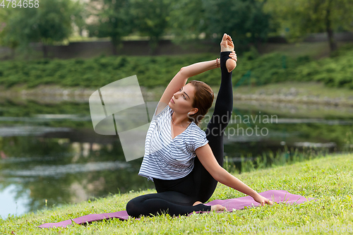 Image of Young beautiful woman doing yoga exercise in green park. Healthy lifestyle and fitness concept.