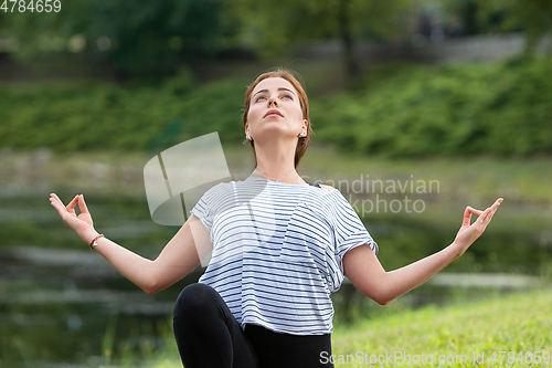 Image of Young beautiful woman doing yoga exercise in green park. Healthy lifestyle and fitness concept.