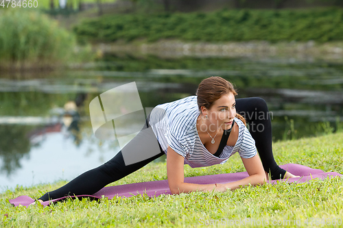 Image of Young beautiful woman doing yoga exercise in green park. Healthy lifestyle and fitness concept.