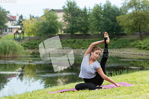 Image of Young beautiful woman doing yoga exercise in green park. Healthy lifestyle and fitness concept.